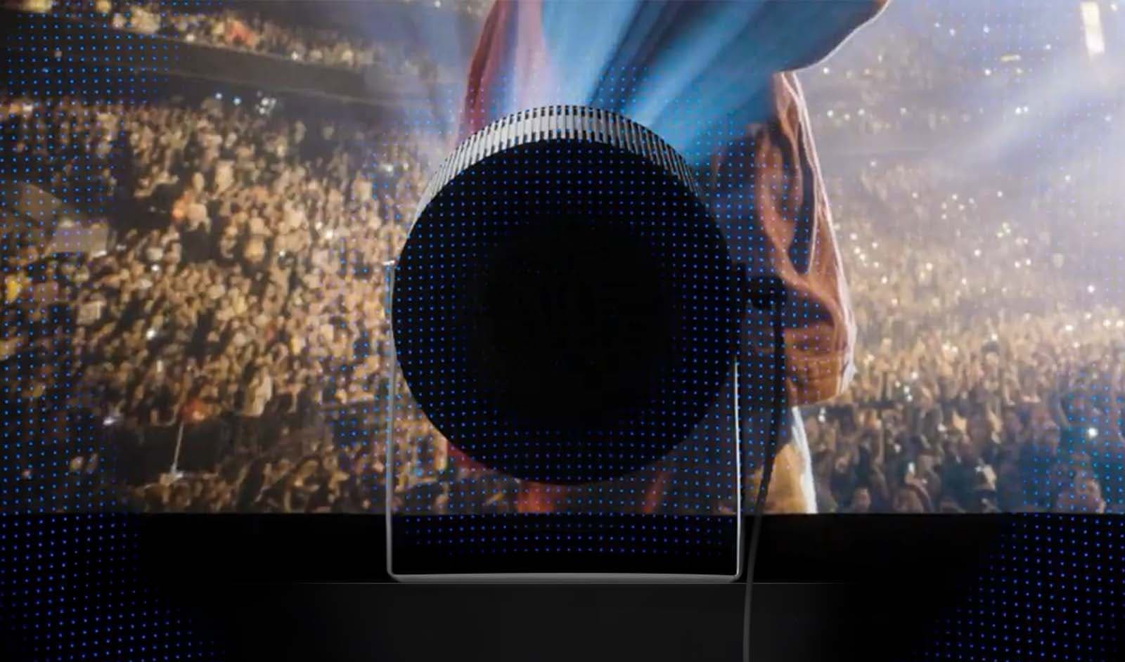 Samsung The Freestyle+ from behind in front of a concert image, illustrating its 360-degree all-around audio