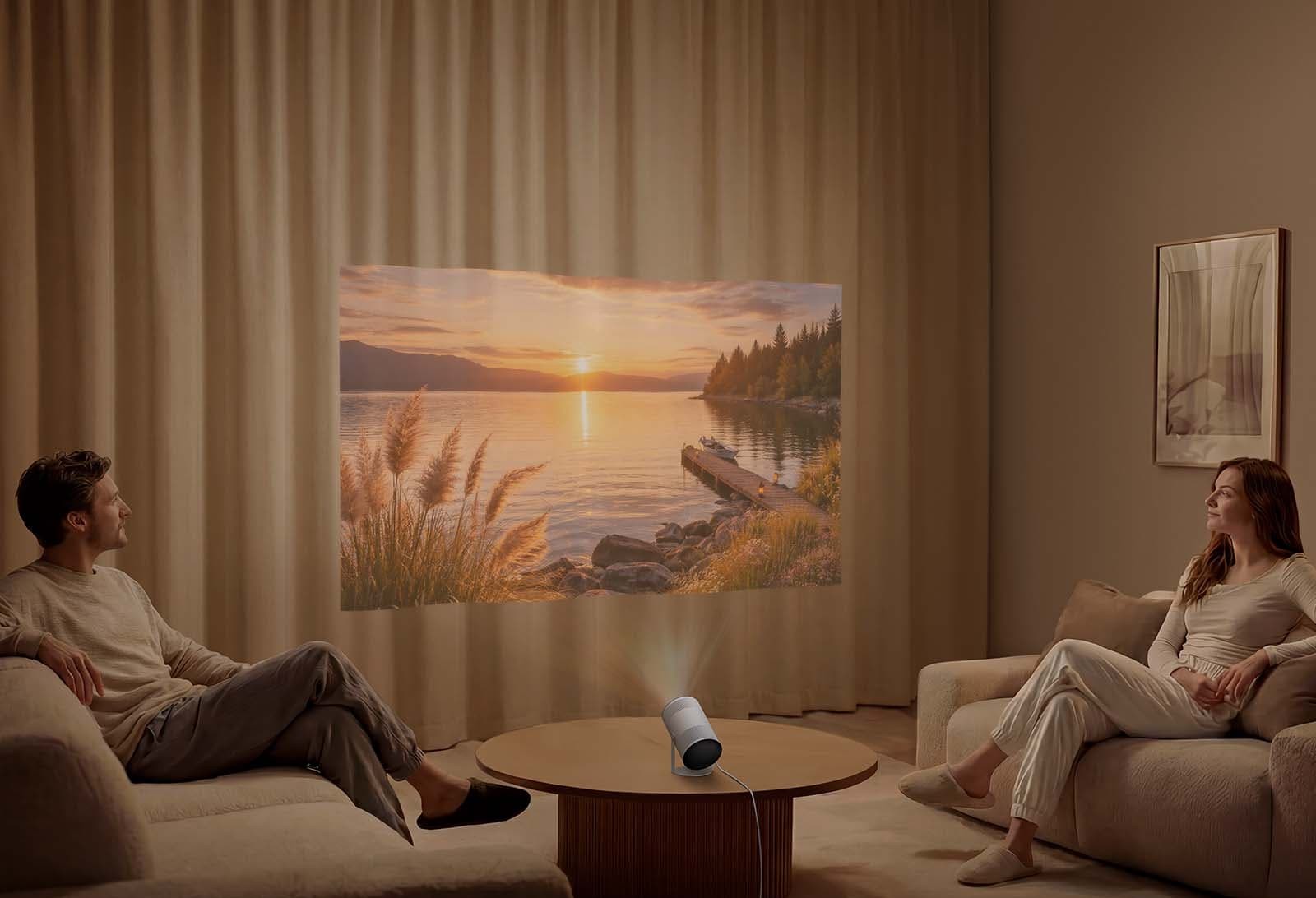 Samsung The Freestyle+ projecting a sunset lake scene onto living room curtains between two sofas