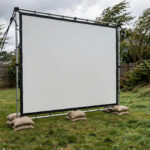 How to Keep Your Outdoor Projector Screen From Blowing in the Wind - 2026 Guide Outdoor projector screen secured with sandbags and ropes